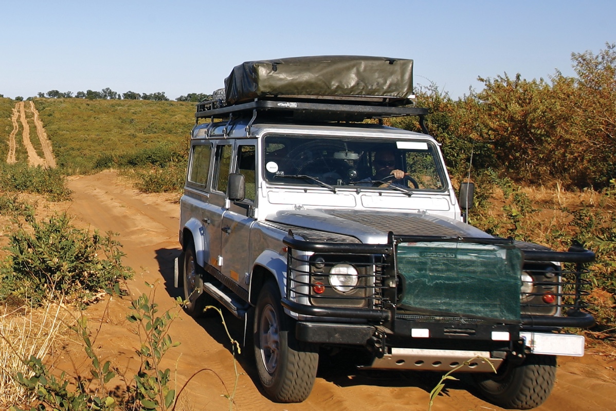 Silver Land Rover Defender with a roof tent driving along a sandy bush track
